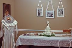 a table with a wedding dress on it and pictures hanging from the wall behind it