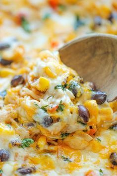 a wooden spoon scooping some food out of a casserole dish with corn and black beans