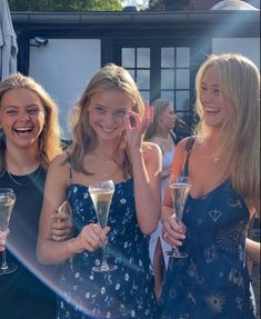 three girls are holding champagne flutes and smiling at the camera while another girl holds her hand up to her face