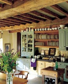 an old fashioned kitchen with green cabinets and white dishes on the counter top, along with a wooden dining room table