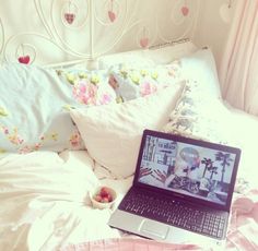 an open laptop computer sitting on top of a bed next to pillows and pink sheets