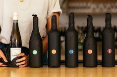 a woman holding a wine bottle in front of six black bottles with different logos on them