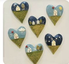 four heart shaped wall hangings with houses and trees painted on the top of them