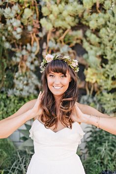 a woman in a white dress holding her hands behind her head and smiling at the camera