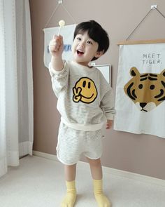 a little boy that is standing up with a toothbrush in his hand and some pictures on the wall behind him