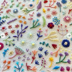 a table topped with lots of different types of embroidered flowers on top of white cloth