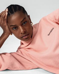 a woman in a pink sweatshirt laying on the ground with her hands behind her head