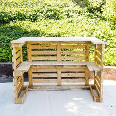 a bench made out of wooden pallets sitting on top of a cement floor next to bushes