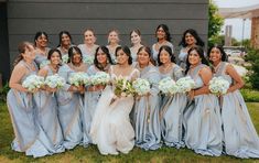 a group of women standing next to each other in front of a building holding bouquets