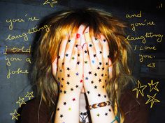 a woman with her hands on her face covered by stars painted on her body and writing on the wall behind her