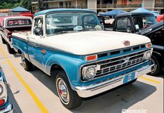 an old blue and white truck parked in a parking lot next to other classic cars