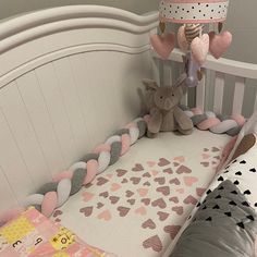 a baby crib with a stuffed animal hanging from it's side, next to a pillow