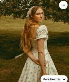 a woman with long red hair wearing a white dress and holding her hands behind her back