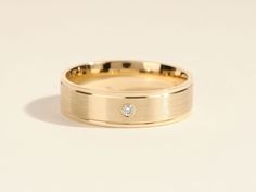 a yellow gold wedding band with a single diamond in the center, on a white background