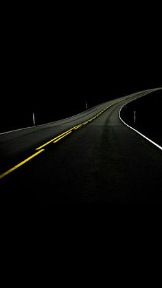 an empty road in the dark with yellow lines on it and a stop sign at the end