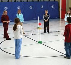 several children are standing in an indoor gym playing with balls and tees on the floor