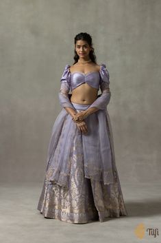 "\nJuliette\u00a0\u00a0\n\nIn an enchanting palette, this lehenga set combines exquisite aari-embroideries and roopa sona zari Kadhua weaves in designs inspired by the ornate and whimsical art and architecture of Rococo. The blouse has a ruched bodice, a classic wide-cut neckline, puffed sleeves, and delicate viscose-organza trimmings along the edges, inspired by the lacework\u00a0which was\u00a0abundantly used\u00a0in Rococo fashion. The gossamer Odhani is\u00a0encrusted with hand-embroidered vines and finished with playful jewel-like tassels.\u00a0\n\n\n Color\u00a0- A\u00a0charming shade of Lavender\n\n Fabric\u00a0- Lehenga skirt in pure satin\u00a0silk, blouse in\u00a0pure\u00a0satin silk with viscose-organza trimmings, and\u00a0Odhani in pure silk organza\u00a0\u00a0\n\nTechnique\u00 Define Feminine, Rococo Fashion, Feminine Wardrobe, Brocade Blouses, Beaded Necklace Designs, Lehenga Skirt, Ruched Bodice, Silk Brocade, Couples Poses For Pictures