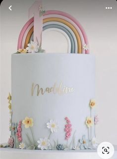 a white cake with flowers and rainbows on it's side that says maddinene