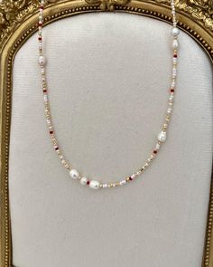 a necklace with pearls and red beads is displayed in a gold frame on a white background