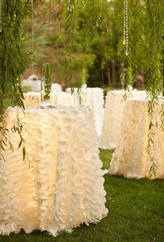 there are many tables covered with white ruffled cloths on the grass and trees in the background