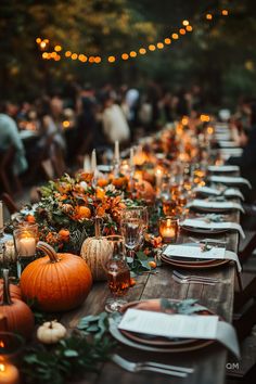 a long table is set with candles and pumpkins for an outdoor dinner party in the woods