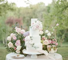 a white wedding cake with pink flowers and greenery on the top is surrounded by champagne glasses