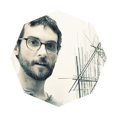 a man with glasses and beard standing in front of a white background that looks like he is looking at the camera