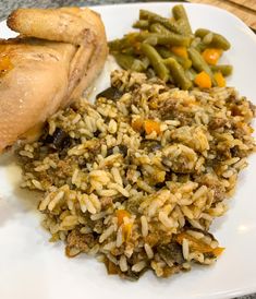 a white plate topped with rice and meat next to green beans on a wooden table