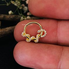 a person holding a gold ring with white stones on it's side, in front of some flowers