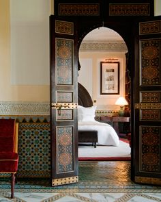 an open door leading to a bedroom with a bed in the background and a red chair next to it