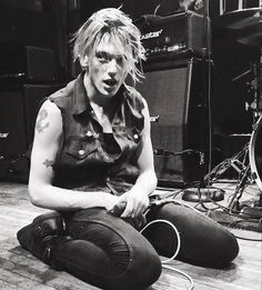 a young man sitting on the floor with his hands in his pockets while playing guitar