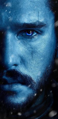 a man with blue eyes looks into the distance in front of snow falling on his face