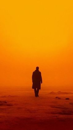 a man walking on the beach at sunset with an orange and yellow sky in the background