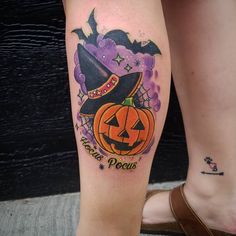 a woman's leg with a tattoo on it and a pumpkin wearing a witches hat