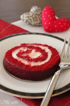 a red velvet cake with white frosting on a plate next to a fork and knife