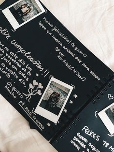 an open black notebook with pictures and writing on it sitting on a white sheet covered bed