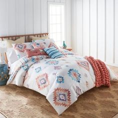 a bedroom with white walls and a large bed covered in colorful comforter sets on top of a rug