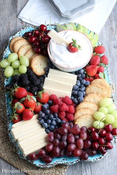 a platter filled with crackers, grapes, strawberries and other fruit on a table