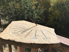 an old roman numeral clock sitting on top of a stone structure in front of trees