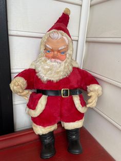 a santa clause doll sitting on top of a red shelf next to a white door