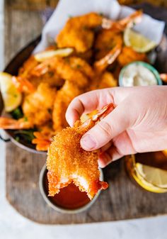 a person holding up a piece of food in front of some dipping sauce and lemon wedges