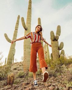 a woman standing in front of a cactus with her arms out and legs spread wide