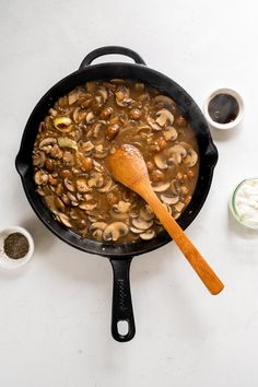 mushrooms are cooking in a skillet with a wooden spoon next to it on a white surface