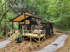 a small cabin in the woods with stairs leading up to it's porch and deck