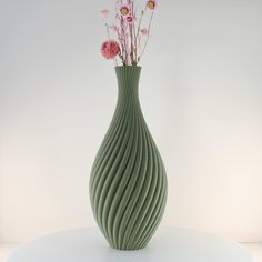 a green vase filled with pink flowers on top of a white table