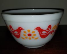 a glass bowl with two birds painted on the side and an orange flower in the middle