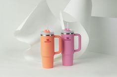 two travel mugs sitting next to each other in front of a white wall and sculpture