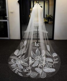 a wedding veil with flowers and leaves on the bottom is displayed in front of a doorway