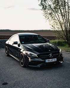 a black mercedes cla parked in a parking lot next to some grass and trees