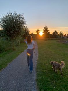 a woman walking her dog on a leash down a path in the park at sunset